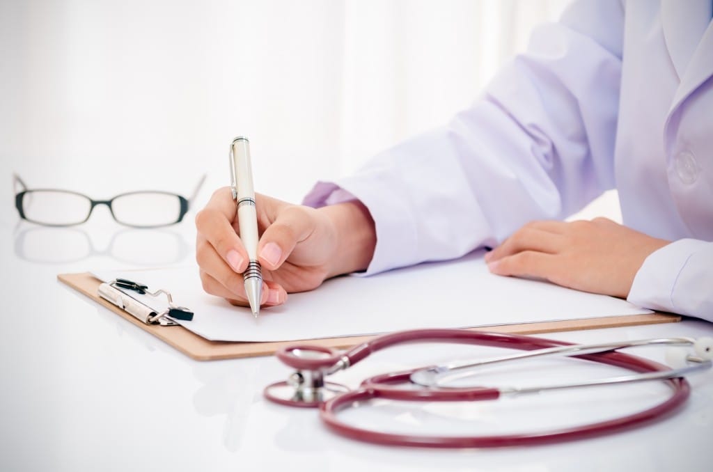 doctor writing record on folder on desk in office
