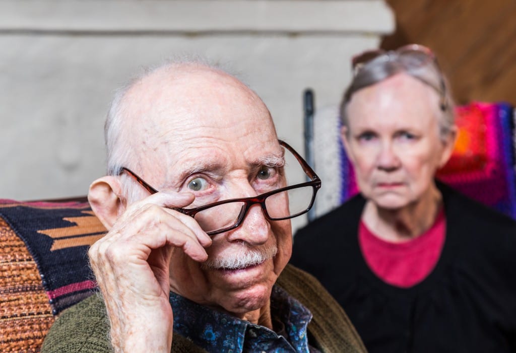 Concerned elderly couple sitting in livingroom scowling